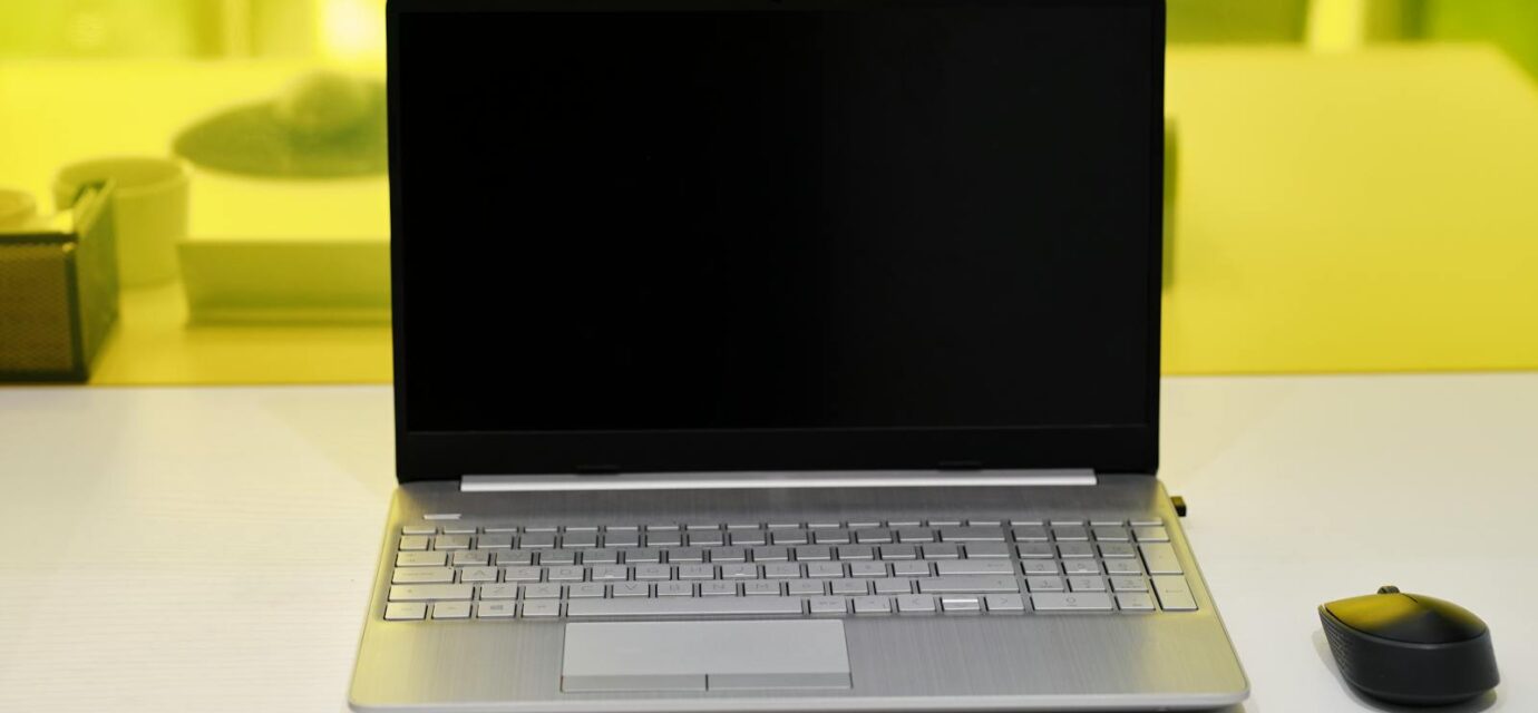 Sleek laptop with a blank screen and wireless mouse on a white desk.