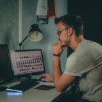 Focused man using a desktop computer in a dimly lit workspace with modern desk setup.