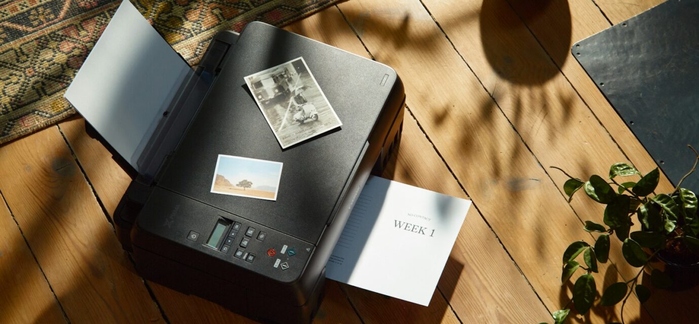 a printer sitting on top of a wooden floor next to a potted plant